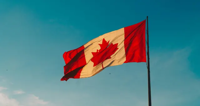 Le drapeau du Canada flottant dans un ciel bleu, symbole de l’immigration fédérale hors Québec